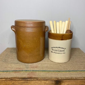 May include: Two brown ceramic jars with lids. The jar on the right has a white label that reads "Fortnum & Mason Ltd. Stilton Cheese 181 Piccadilly W1".
