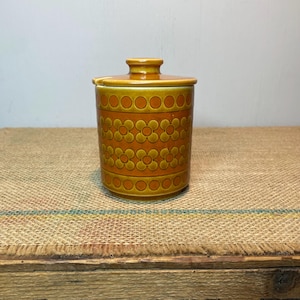 May include: A brown and orange ceramic sugar bowl with a lid. The bowl features a floral pattern with yellow and orange flowers.