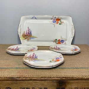May include: A set of vintage floral patterned porcelain plates and a serving tray. The plates are octagonal and have a gold rim. The tray has a gold rim and handles.