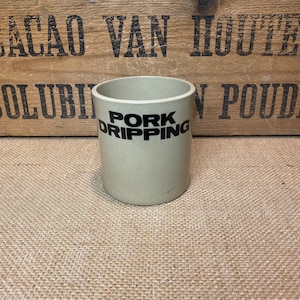 May include: A beige ceramic jar with black lettering that reads "PORK DRIPPING" on a hessian background.