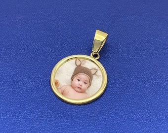 May include: Gold-toned pendant with a round photo insert featuring a baby wearing a brown and white deer hat.