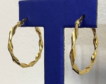 May include: A pair of gold hoop earrings with a twisted design. The earrings are displayed on a blue stand.