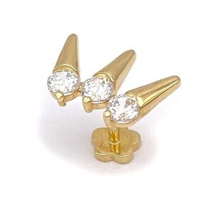 May include: Gold body jewelry with three clear round stones and three gold spikes.