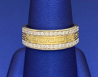 May include: A gold band ring with a Greek key design and a row of small diamonds around the edge.