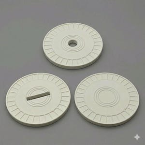 May include: Three off-white, circular objects with a ridged outer edge and a central design. One has a hole, another a slot, and the third a raised circle. The objects are arranged on a gray background.