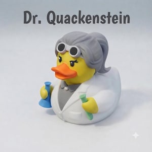Könnte beinhalten: Eine gelbe Quietscheente mit der Aufschrift Dr. Quackenstein, mit grauem Haar zum Pferdeschwanz gebunden, weißer Schutzbrille, weißem Laborkittel über einem grauen Hemd, die einen blauen Erlenmeyerkolben und ein grünes Reagenzglas hält.