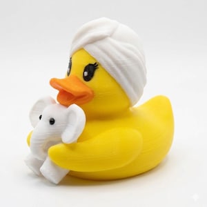 May include: A yellow rubber duck wearing a white spa turban, clutching a small white elephant. The duck has an orange beak and black eyes with eyelashes. A fun, spa-themed bath toy.