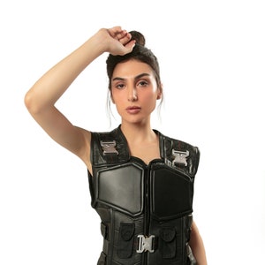 May include: A black leather vest with multiple pockets and silver buckles. The vest has a zipper closure and a padded front.