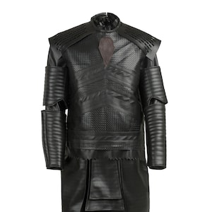 Puede incluir: Traje de cuero negro con un diseño texturizado. El traje presenta una falda larga y fluida y una parte superior ajustada con cuello alto. La parte superior tiene un diseño decorativo en el pecho.