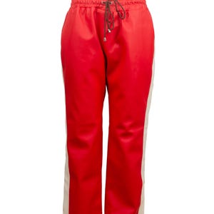 May include: Red athletic pants with a drawstring waist and cream-colored side stripes. The pants have a relaxed fit and are made of a smooth, shiny material. A stylish and comfortable addition to any wardrobe.