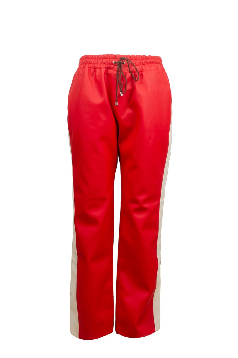 May include: Red athletic pants with a drawstring waist and cream-colored side stripes. The pants have a relaxed fit and are made of a smooth, shiny material. A stylish and comfortable addition to any wardrobe.