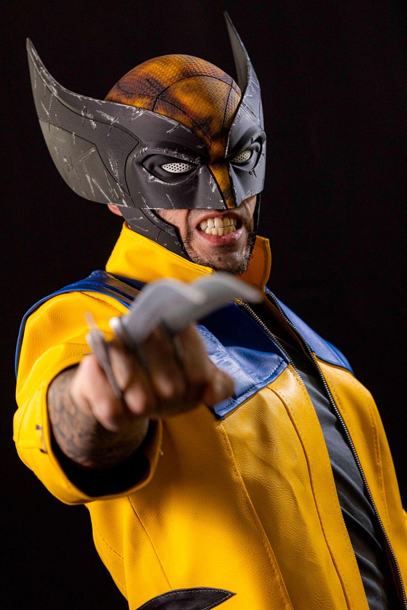 May include: A person wearing a yellow and blue leather jacket with a black and gray mask. The person is holding a silver claw in their right hand. The person is looking at the camera with a fierce expression.