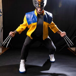 May include: A person dressed as Wolverine, wearing a yellow and blue jacket, black pants, and white sneakers. The person is holding silver claws in each hand and has a black and yellow mask on.