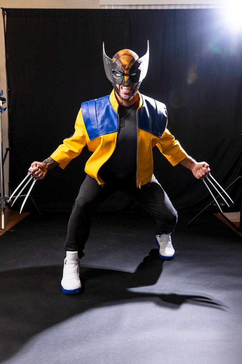 May include: A person dressed as Wolverine, wearing a yellow and blue jacket, black pants, and white sneakers. The person is holding silver claws in each hand and has a black and yellow mask on.