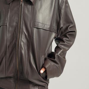 May include: A brown leather bomber jacket with a zipper closure and a ribbed waistband.