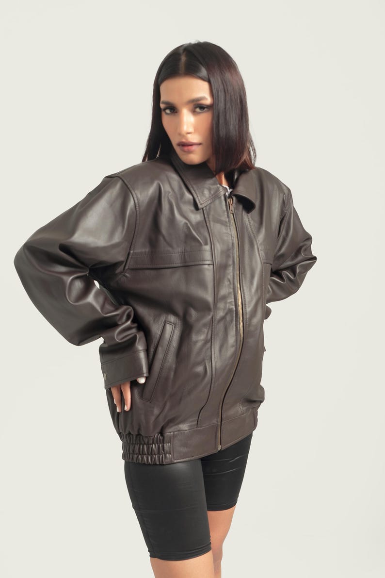 May include: A brown leather jacket with a zipper closure and a stand-up collar. The jacket has a relaxed fit and a slightly cropped length.