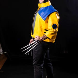 May include: A person dressed as Wolverine, wearing a yellow and blue costume with a black mask and holding silver claws. The costume has a blue and yellow X-Men logo on the left sleeve.