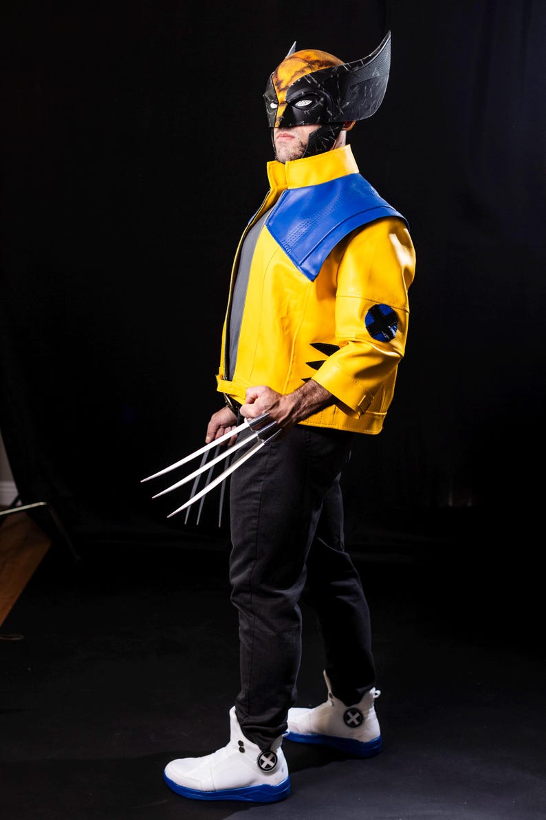 May include: A person dressed as Wolverine, wearing a yellow and blue costume with a black mask and holding silver claws. The costume has a blue and yellow X-Men logo on the left sleeve.