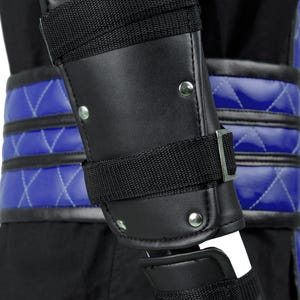 Puede incluir: Protecci&oacute;n de brazo de cuero negro con correas ajustables y remaches plateados. La protecci&oacute;n se lleva sobre una tela acolchada azul.