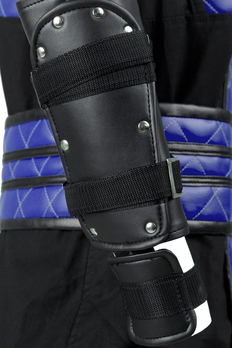 Puede incluir: Protecci&oacute;n de brazo de cuero negro con correas ajustables y remaches plateados. La protecci&oacute;n se lleva sobre una tela acolchada azul.