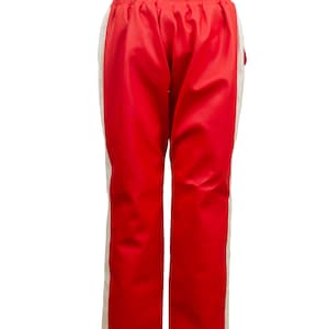 May include: Red athletic pants with a white stripe down the side. The pants have an elastic waistband. The material has a slight sheen. These pants are suitable for sports or casual wear.