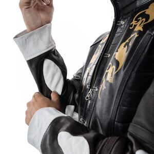 May include: A brown leather jacket with white accents and gold embroidery. The jacket has a zipper closure and a stand-up collar.