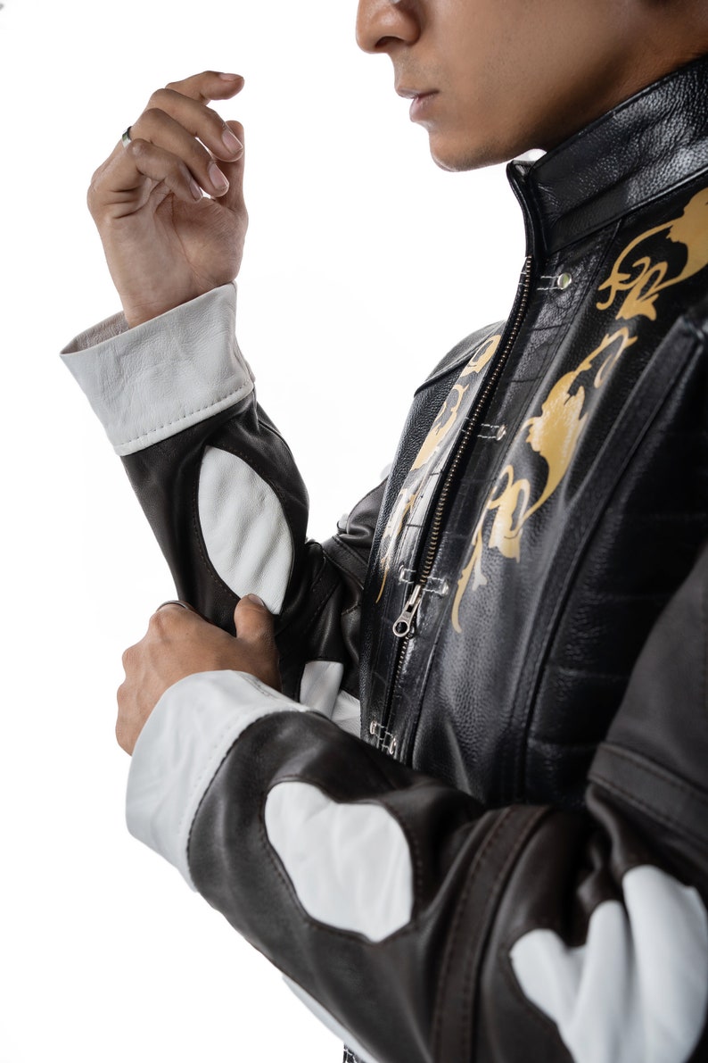 May include: A brown leather jacket with white accents and gold embroidery. The jacket has a zipper closure and a stand-up collar.