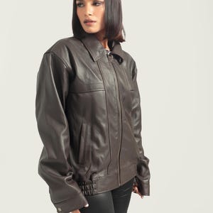 May include: A brown leather jacket with a zipper closure and a ribbed waistband. The jacket has a collar and two pockets.