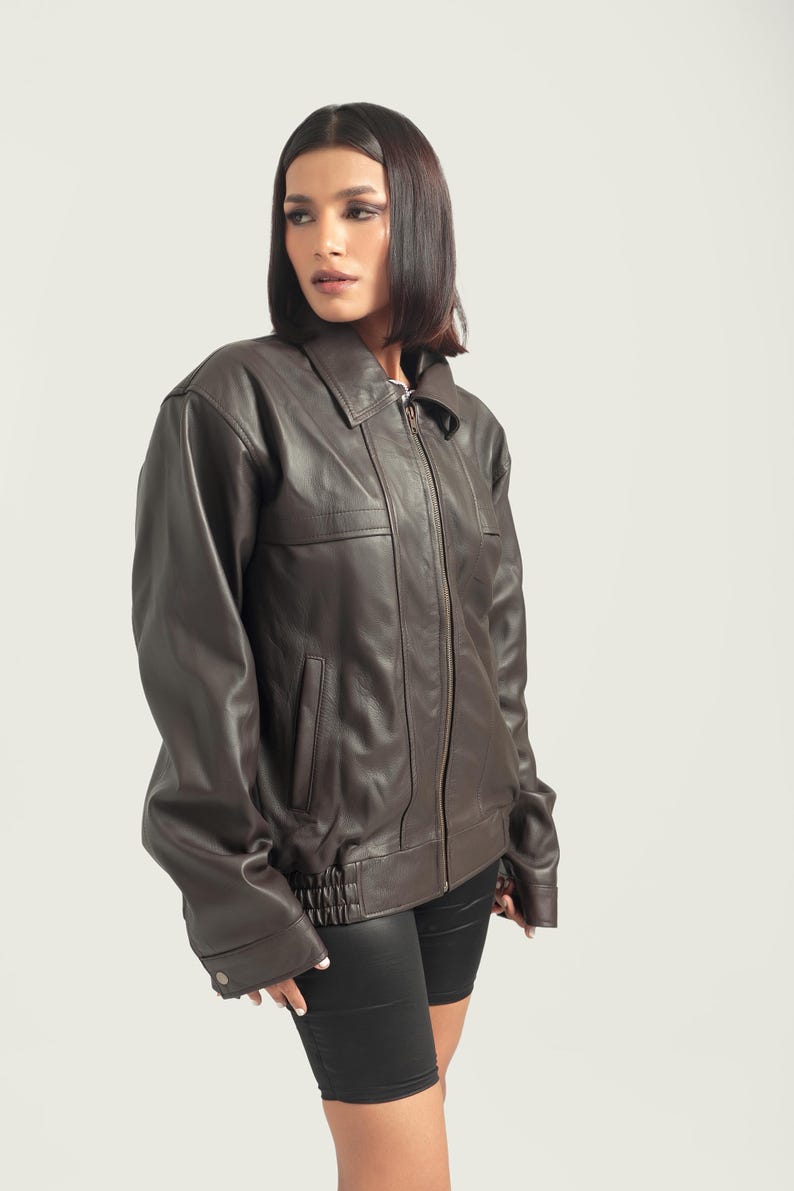 May include: A brown leather jacket with a zipper closure and a ribbed waistband. The jacket has a collar and two pockets.