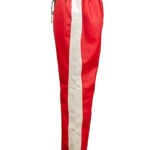 May include: Red athletic pants with a wide white stripe down the side. The pants have a drawstring waist and a smooth, satin-like texture. These pants are a stylish addition to any wardrobe.