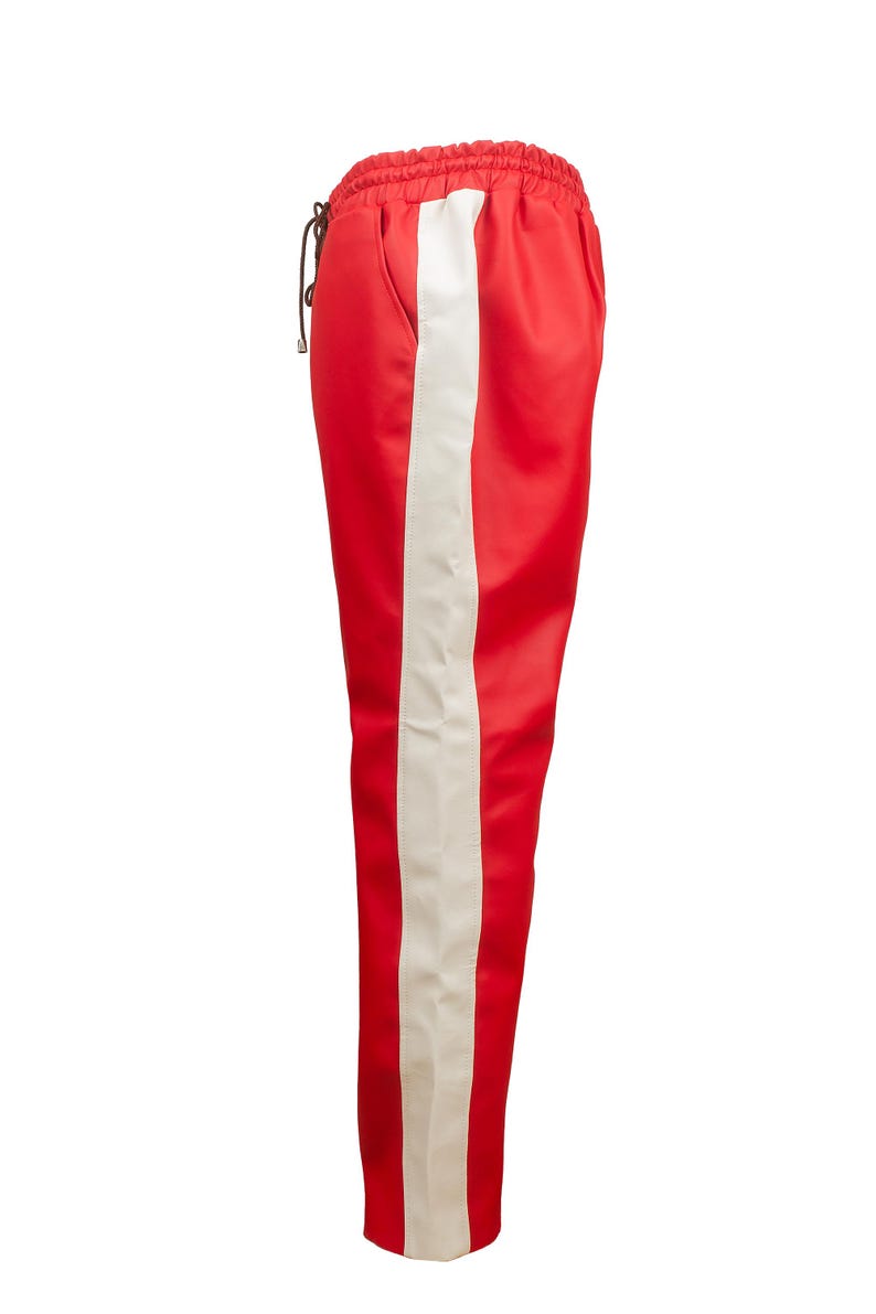 May include: Red athletic pants with a wide white stripe down the side. The pants have a drawstring waist and a smooth, satin-like texture. These pants are a stylish addition to any wardrobe.
