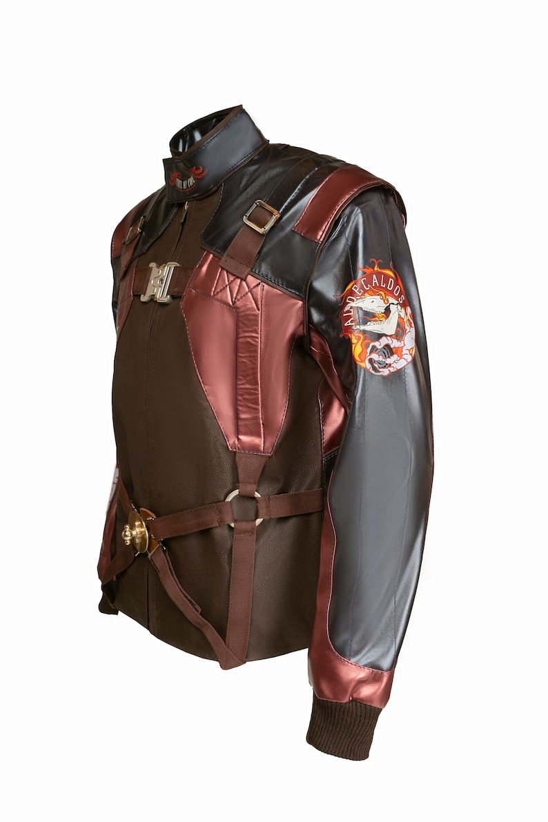 Puede incluir: Una chaqueta de cuero marr&oacute;n y burdeos con un parche negro y plateado en la manga que dice "ALDRECALDOS". La chaqueta tiene un cuello alto y una cremallera. Presenta un dise&ntilde;o &uacute;nico con correas y hebillas.