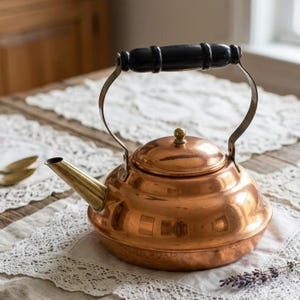 May include: A polished copper tea kettle with a rounded body, a short angled spout, and a domed lid. The kettle features a curved metal handle topped with a smooth, cylindrical black wooden grip, providing a contrast to the metallic finish.