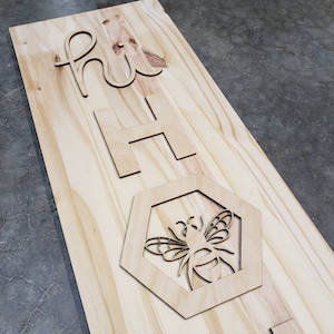 May include: A wooden sign with the words "hi ho" cut out in the wood. Below the words is a cutout of a bee inside a hexagon.