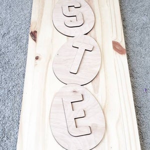 May include: A wooden sign with the word "happy" and the word "easter" spelled out in individual letters on a light brown background.