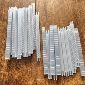K&ouml;nnte beinhalten: Zwei Stapel hellblauer, rechteckiger Kunststoffteile mit verschiedenen strukturierten Mustern. Die Teile sind vertikal angeordnet, einige mit einem gitterartigen Design und andere mit einem diagonalen Muster. Die Teile liegen auf einer Holzoberfl&auml;che.