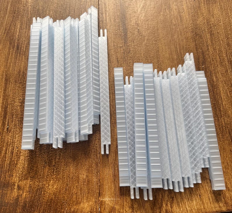 K&ouml;nnte beinhalten: Zwei Stapel hellblauer, rechteckiger Kunststoffteile mit verschiedenen strukturierten Mustern. Die Teile sind vertikal angeordnet, einige mit einem gitterartigen Design und andere mit einem diagonalen Muster. Die Teile liegen auf einer Holzoberfl&auml;che.