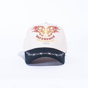 May include: Cream-colored baseball cap with a black brim and barbed wire embroidery. The cap features a design with two flaming skulls and the text "REFERENCE BORN TO WIN RALLY 2020".