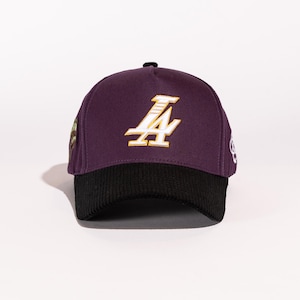 May include: A purple and black baseball cap with a gold and white "LA" logo on the front.