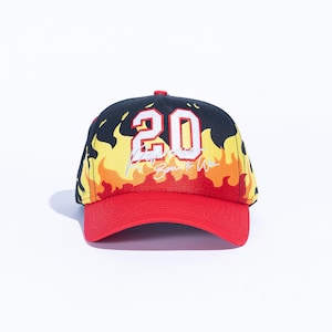 May include: A black and red baseball cap with a flame design. The cap features the number "20" in white, along with the text "Born to Win". The brim and button are red.