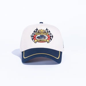 May include: Cream-colored baseball cap with a navy blue brim and gold trim. The cap features a colorful embroidered patch with the text "REFERENCE SPEEDWAY LOS ANGELES, CA" and a race car graphic, along with checkered flags.