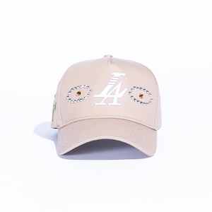 May include: Tan baseball cap with the white letter "A" and the number "4" on the front. The cap has rhinestone and gold stud accents around the logo. The cap is a neutral color and has a curved brim.
