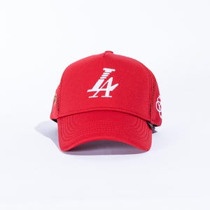 May include: Red trucker cap with a white logo on the front. The cap has a mesh back and a curved peak. The logo is a stylized white number 4 with a design above it. The cap is a solid red colour.
