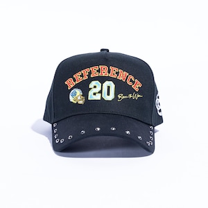 May include: Black baseball cap with the word "REFERENCE" in orange and "20" in light blue. The cap features a football helmet graphic and the text "Born to Win". Silver studs line the brim.