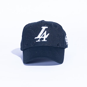 May include: A navy blue baseball cap with a paisley pattern and the white letters "LA" on the front. The cap has a curved brim and a white emblem on the side. The hat is set against a white background.