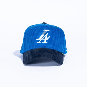 May include: Blue corduroy baseball cap with a navy blue brim. The cap features a white logo on the front. The hat is a classic style, suitable for casual wear.