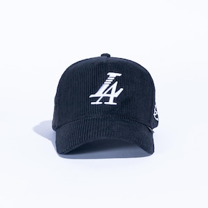 May include: Black corduroy baseball cap with a white embroidered "LA" logo on the front. The cap has a curved brim and a six-panel design. A small white emblem is on the side.