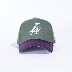 May include: Olive green baseball cap with a purple brim and white embroidered "LA" logo. The cap features a curved brim and a white interior. A small graphic is visible on the side.
