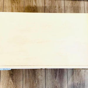 May include: A white wooden coffee table with a simple design. The table has a rectangular top and a slightly raised edge.