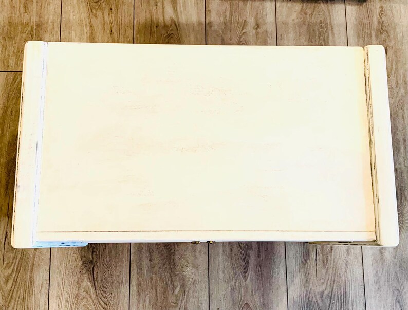 May include: A white wooden coffee table with a simple design. The table has a rectangular top and a slightly raised edge.